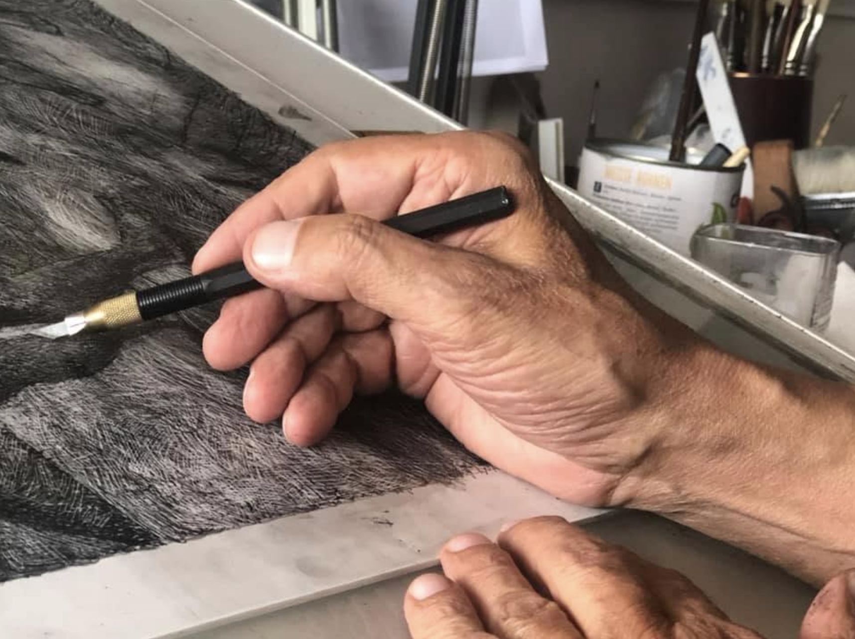 Close-up of Fidel Regueros' hands drawing with a fine blade, cross-hatching a charcoal drawing